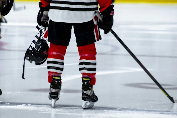 Eishockeyspieler mit Schläger und Helm in der Hand auf dem Eis